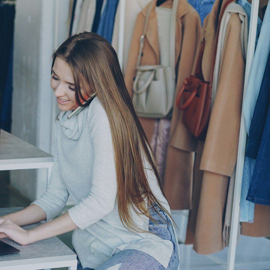Une commerçante au travail sur son ordinateur portable, entre les vêtements de sa boutique
